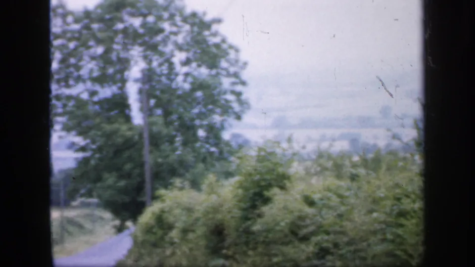 Soft 8mm view of a rural English lane, hedges, and trees seen through a dark frame edge.