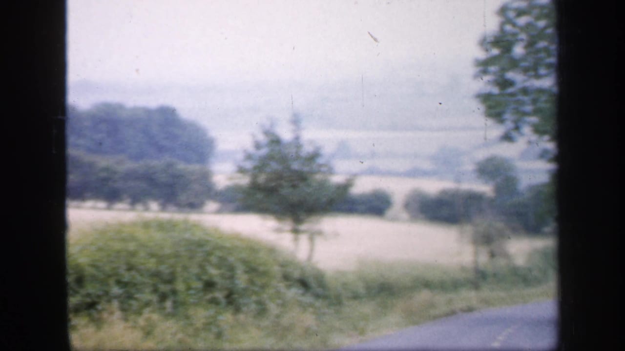 Soft rural view with hedges, fields, tree line, and a dark film-frame divider.