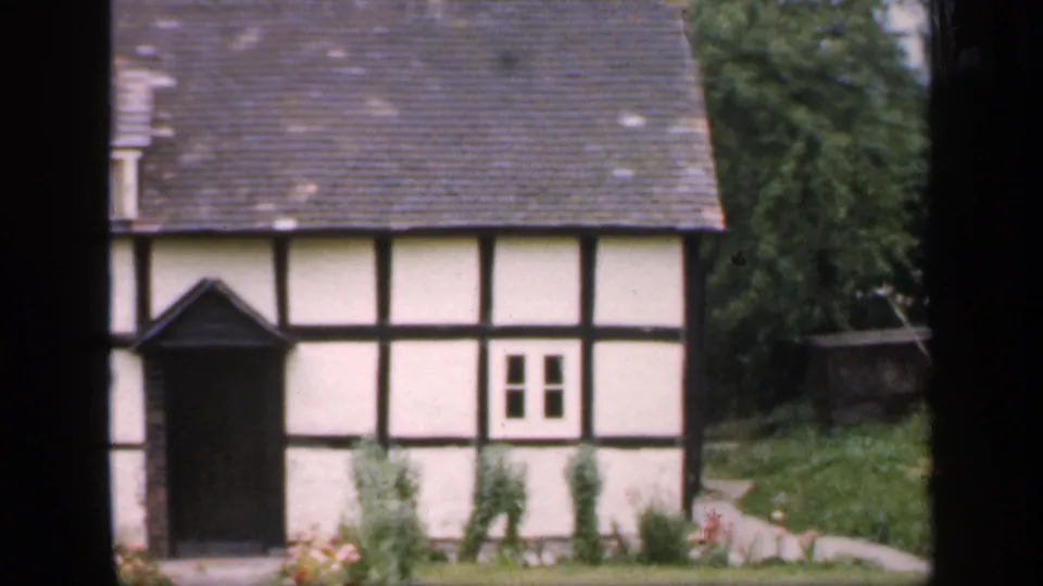 1949 England frame of a traditional half-timbered cottage with white plaster walls, dark beams, tiled roof, and a small garden.
