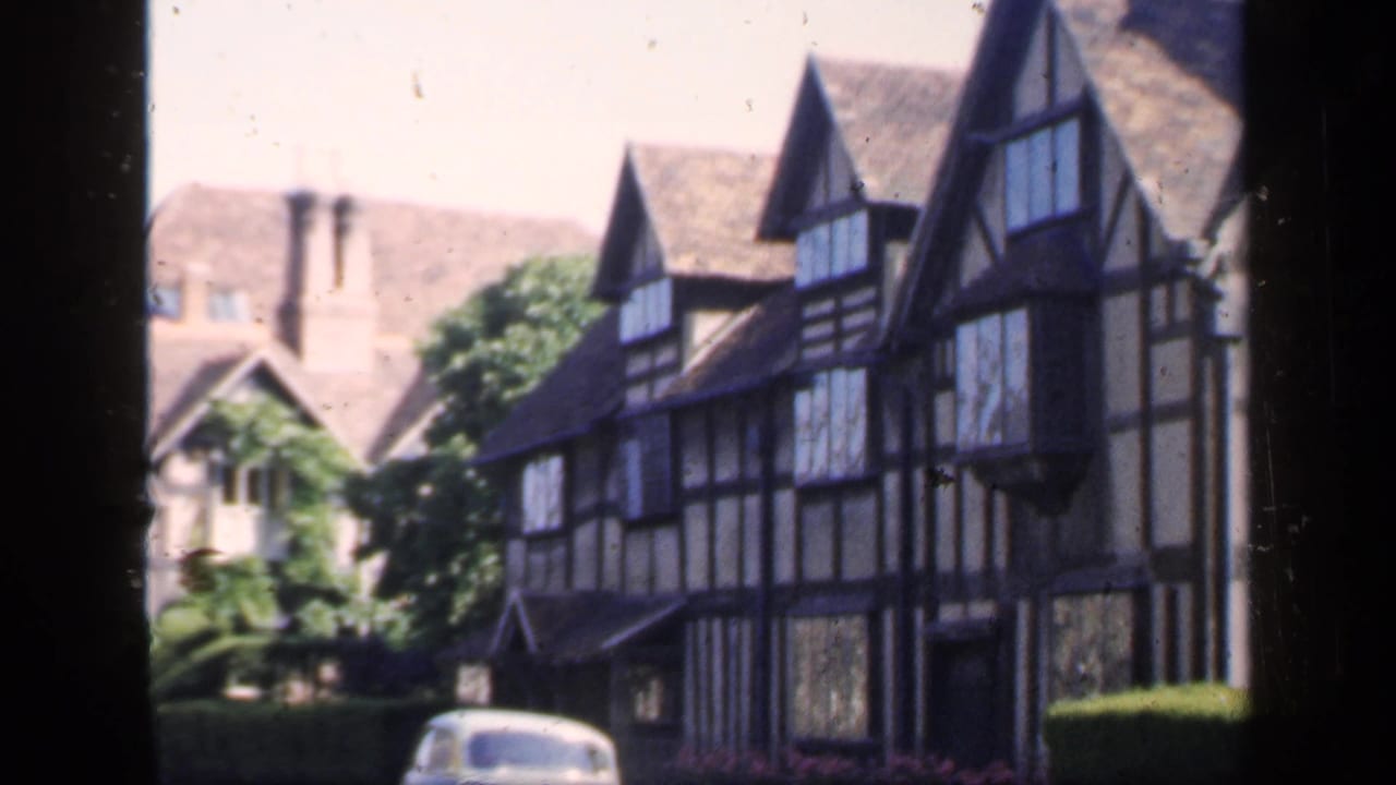 Timber-framed houses seen through dark window edges with a small car partly visible at street level.