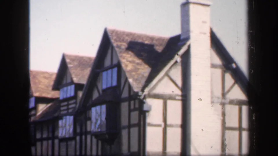 1949 England frame showing half-timbered house elevations, steep tiled roofs, gabled windows, and a tall pale chimney at the right side.