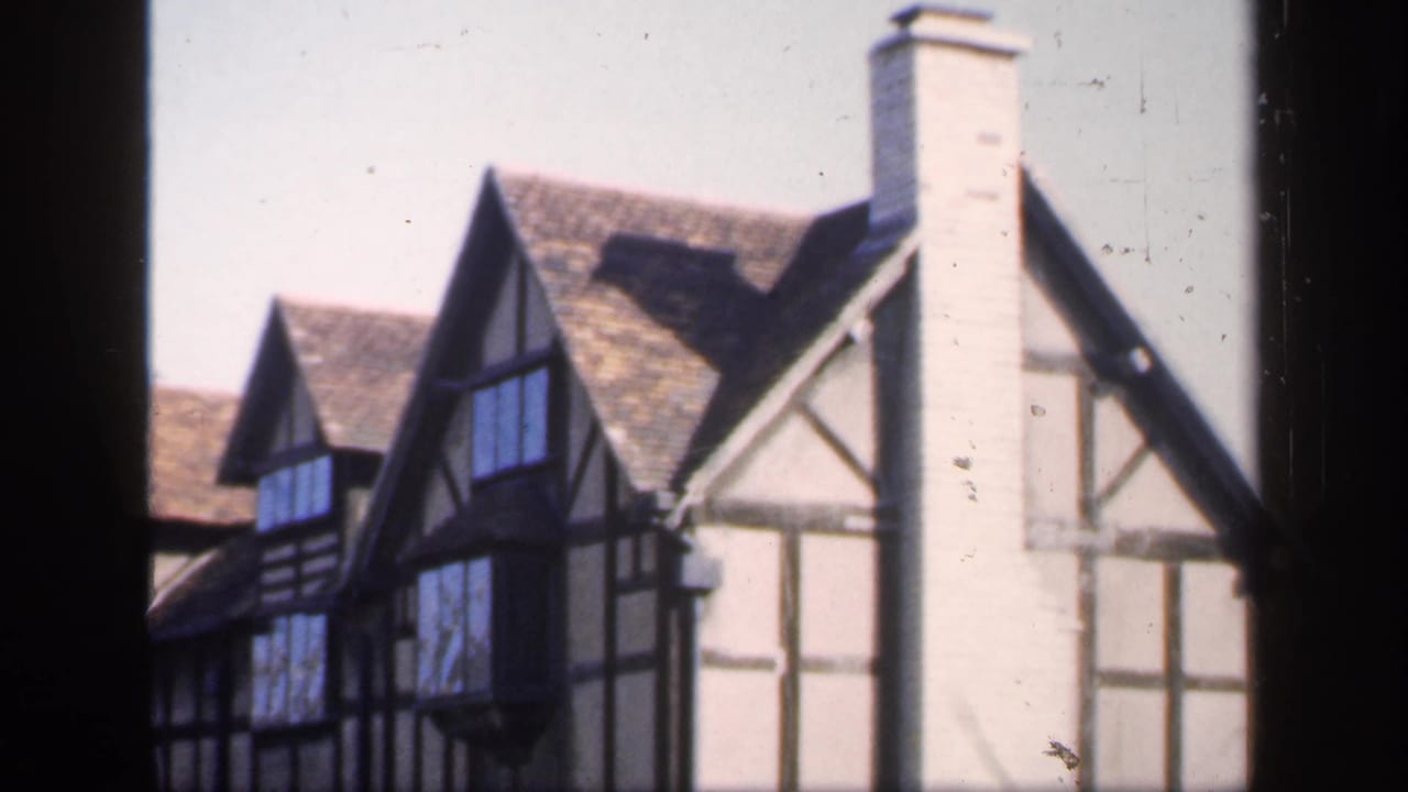 Tudor-style houses with timber framing, steep roofs, and tall chimneys seen through a dark foreground frame.