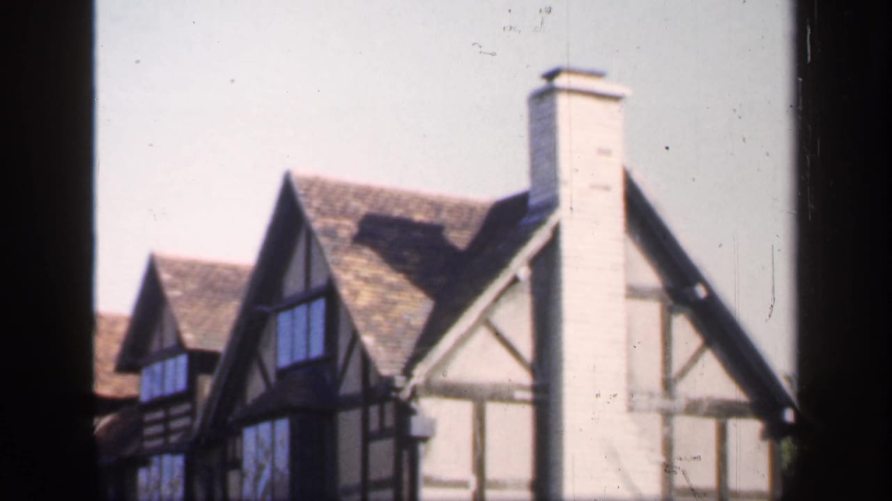 Row of Tudor-style house fronts with gables, dark windows, and a tall chimney beside a dark vertical frame.
