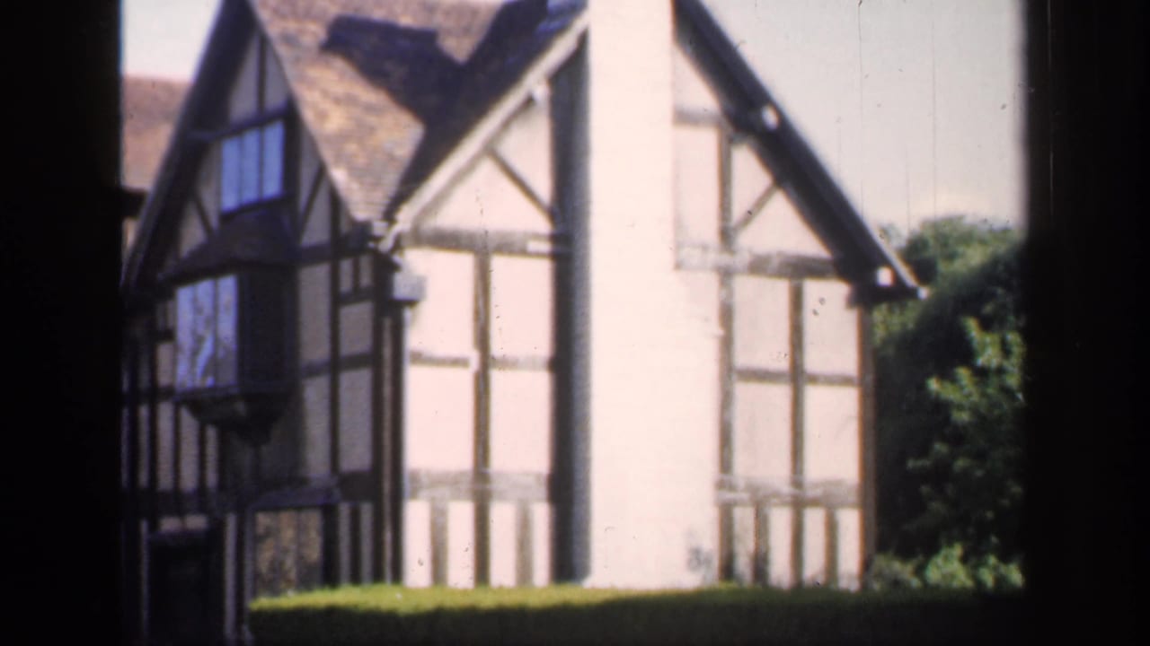 1949 England 8mm frame showing a black-and-white timber-framed house viewed through dark foreground window bars.