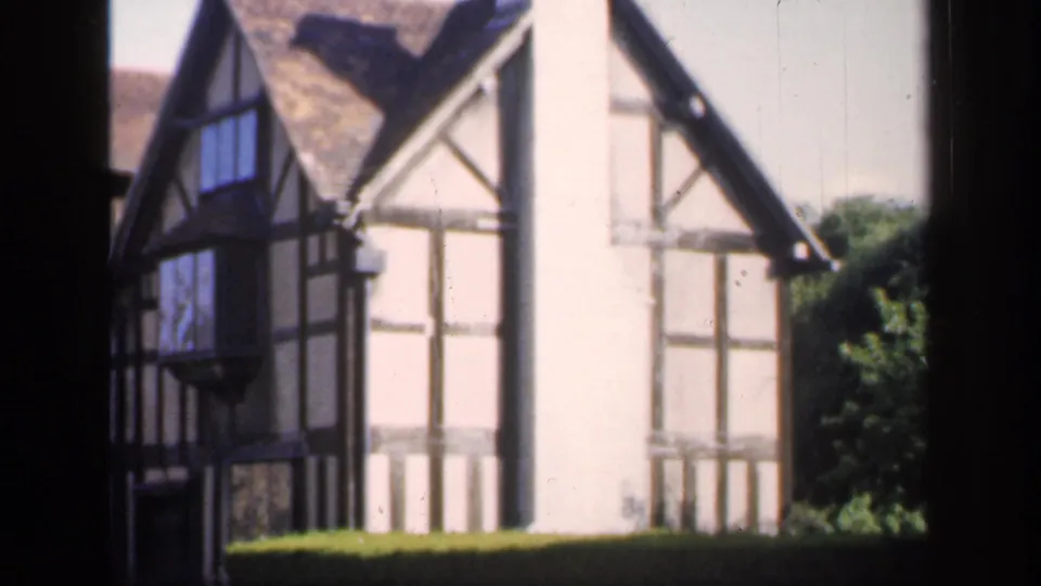 1949 England 8mm frame showing a black-and-white timber-framed house viewed through dark foreground window bars.