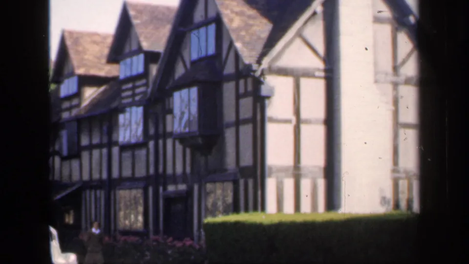 1949 England frame showing the timber-framed house and hedge, with a small distant person visible near the lower doorway area.