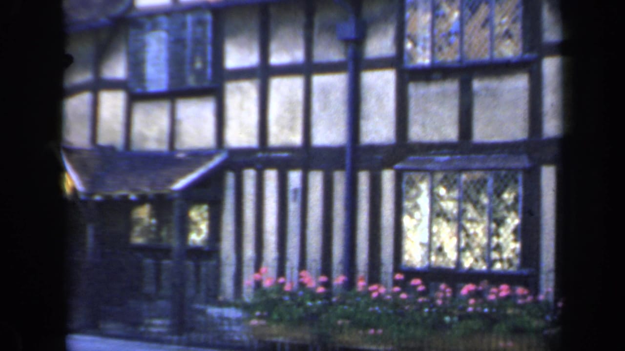 1949 England frame with the camera panning across a Tudor-style exterior, showing leaded glass, flower boxes and the edge of a gabled entrance.