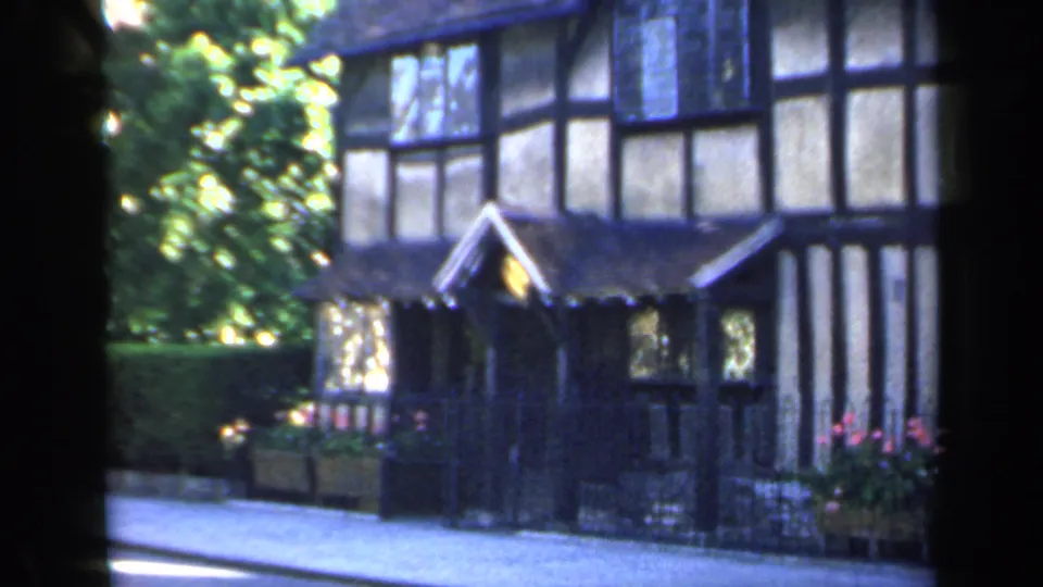 1949 England frame showing the manor entrance area, with a dark gabled porch, leaded windows, half-timbered walls and greenery to the side.