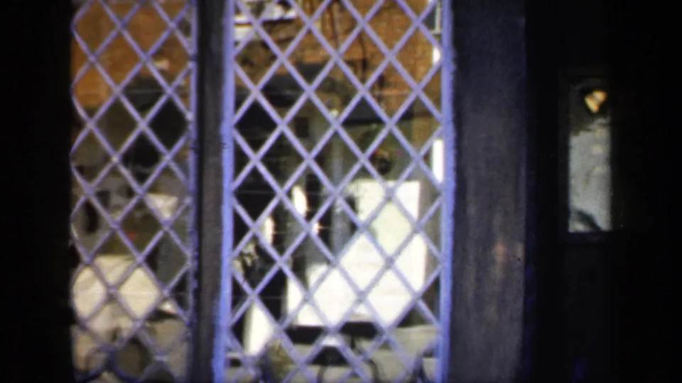 1949 England 8mm frame showing dark woodwork, a small door panel, and leaded windows at the Shakespeare birthplace site.