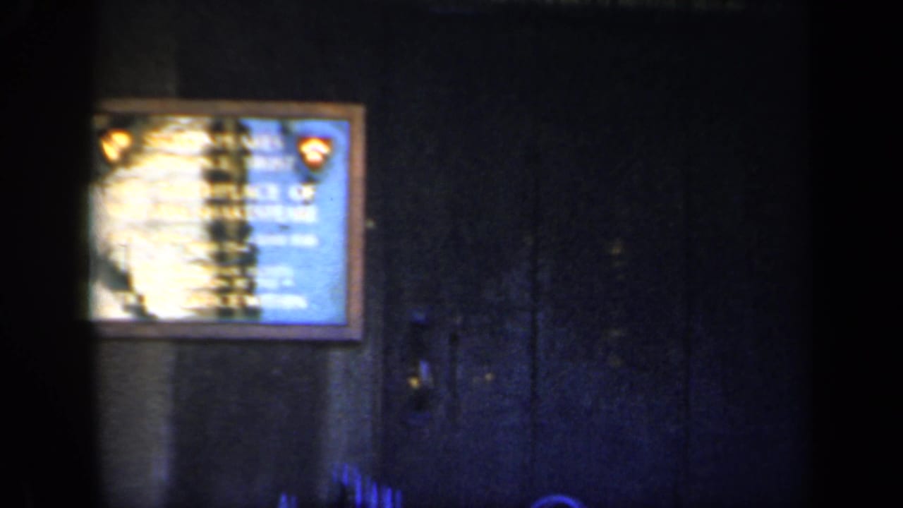 Framed plaque on a dark wall, partly obscured by shadow and film blur.