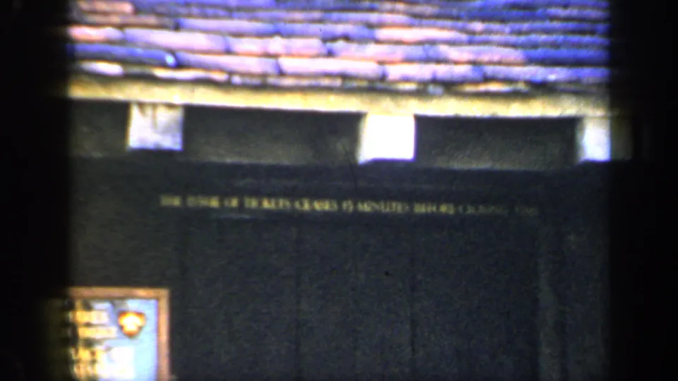 1949 England 8mm frame showing a dark historic building facade, tiled roof and posted ticket-closing notice.