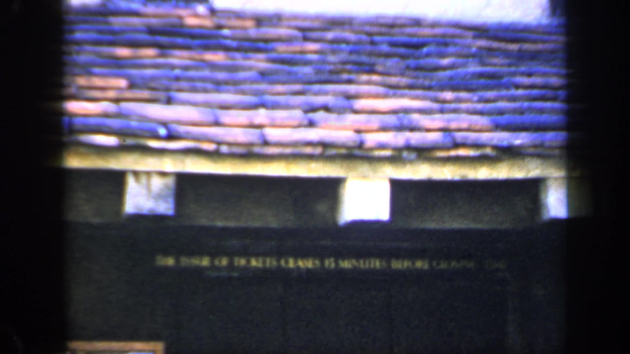 1949 England 8mm frame with terracotta-blue roof tiles and a dark facade carrying a ticket-closing notice.