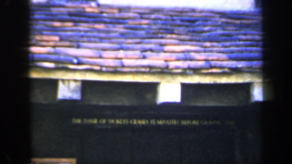 1949 England 8mm frame with terracotta-blue roof tiles and a dark facade carrying a ticket-closing notice.