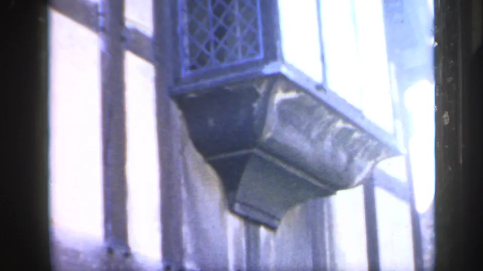 1949 England 8mm frame showing a leaded diamond-paned window, drainpipe and projecting exterior detail.