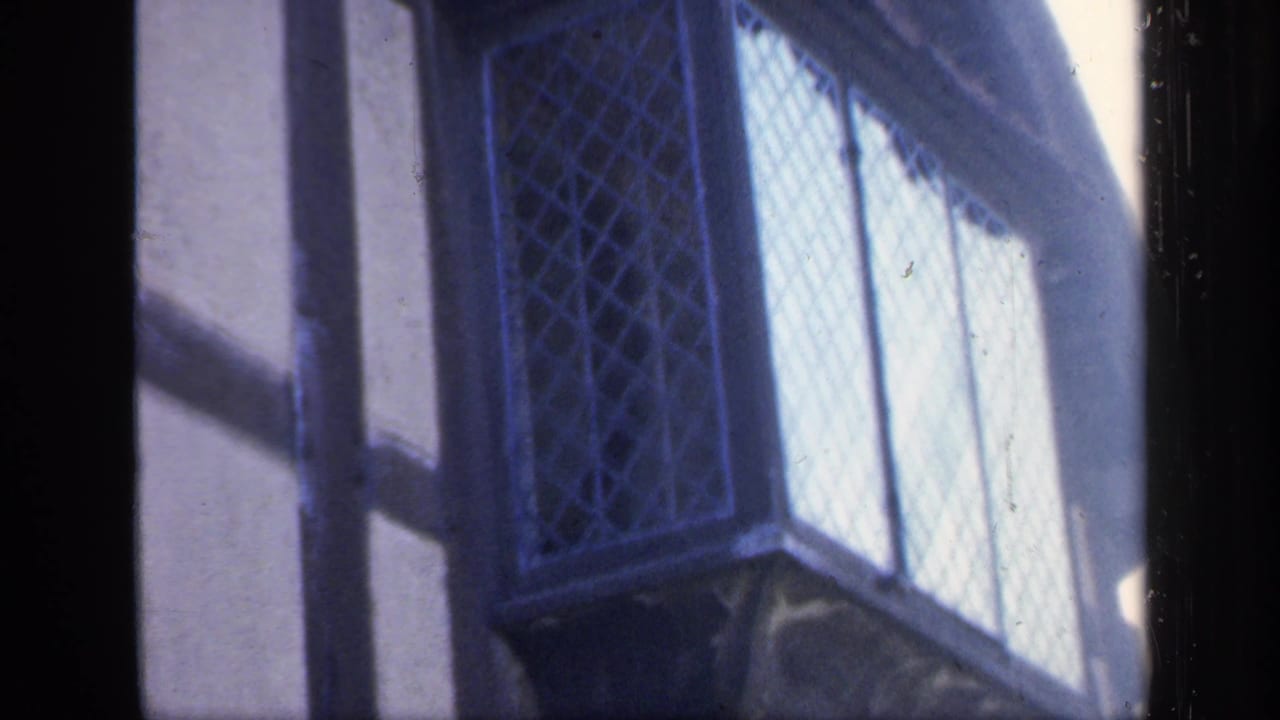 1949 England home-movie frame showing a close exterior view of timber framing and leaded diamond windows.