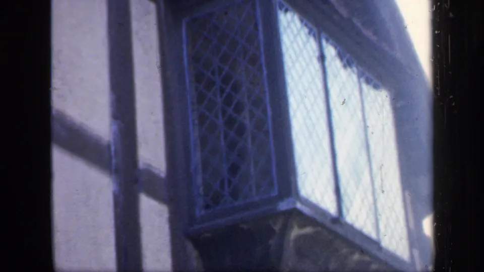 1949 England home-movie frame showing a close exterior view of timber framing and leaded diamond windows.