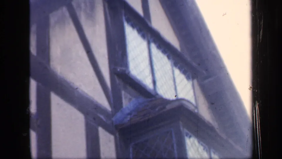 1949 England home-movie still focusing on a projecting leaded window bay and dark timber patterning.