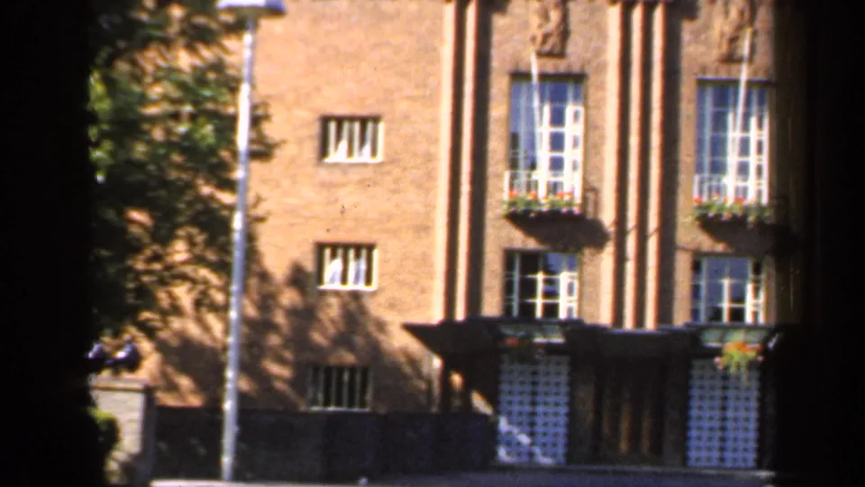 1949 England frame showing the building entrance, white-framed windows, flower boxes, and brick vertical details.