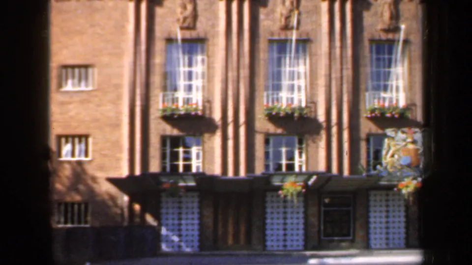 1949 England home-movie frame with flower-box windows, a formal entrance, and a decorative crest on the brick facade.