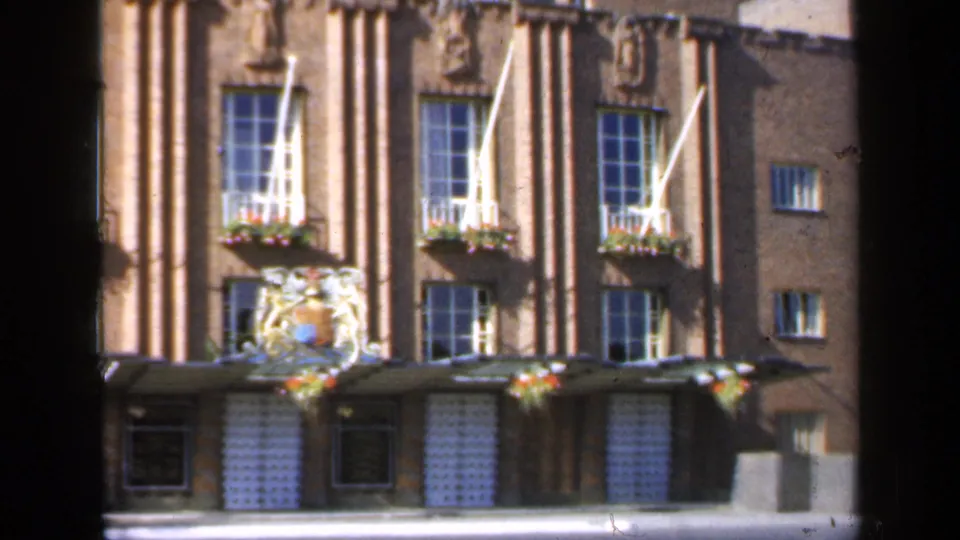 1949 England 8mm view of the building entrance area, with a crest above the doorway, flower boxes under windows and strong foreground obstruction.