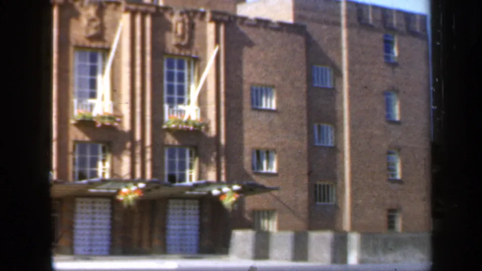Final 1949 England frame showing the brick facade shifting right, with windows, flower boxes, a crest and an adjoining plain brick wall.