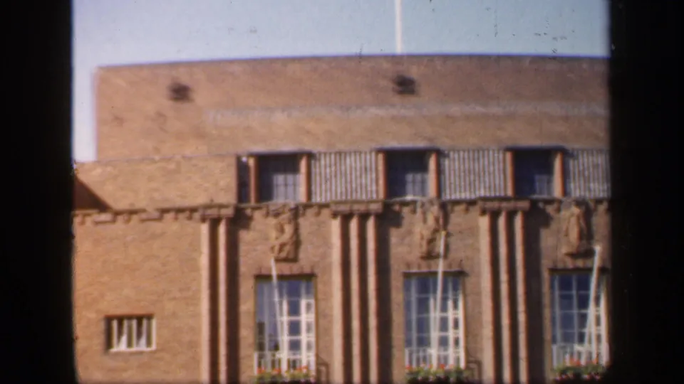 1949 England home-movie view of the building facade, showing tall lower windows, flower boxes, relief figures and a small side window.