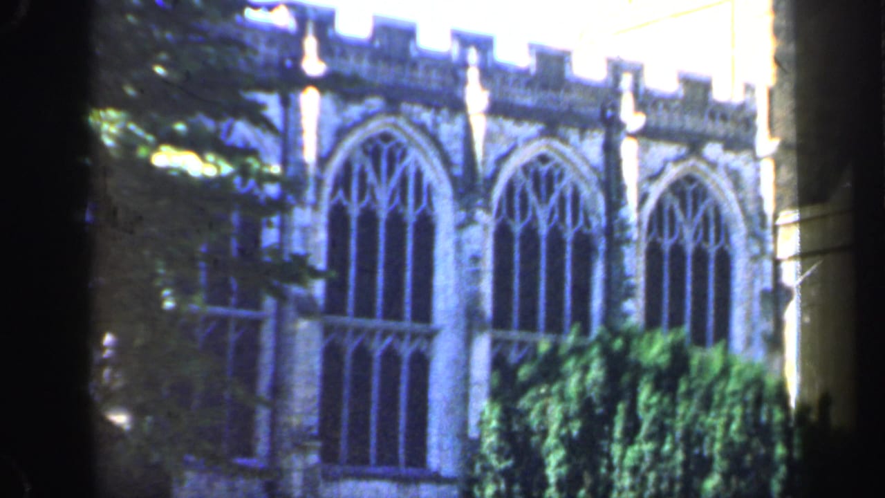 Stone church wall with tall Gothic arched windows, foliage, and dark foreground framing.