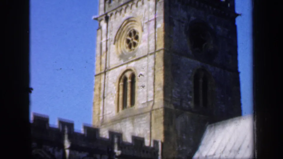 1949 England frame centered on the church tower, showing a circular window, arched openings, weathered stone, and the adjoining roofline.
