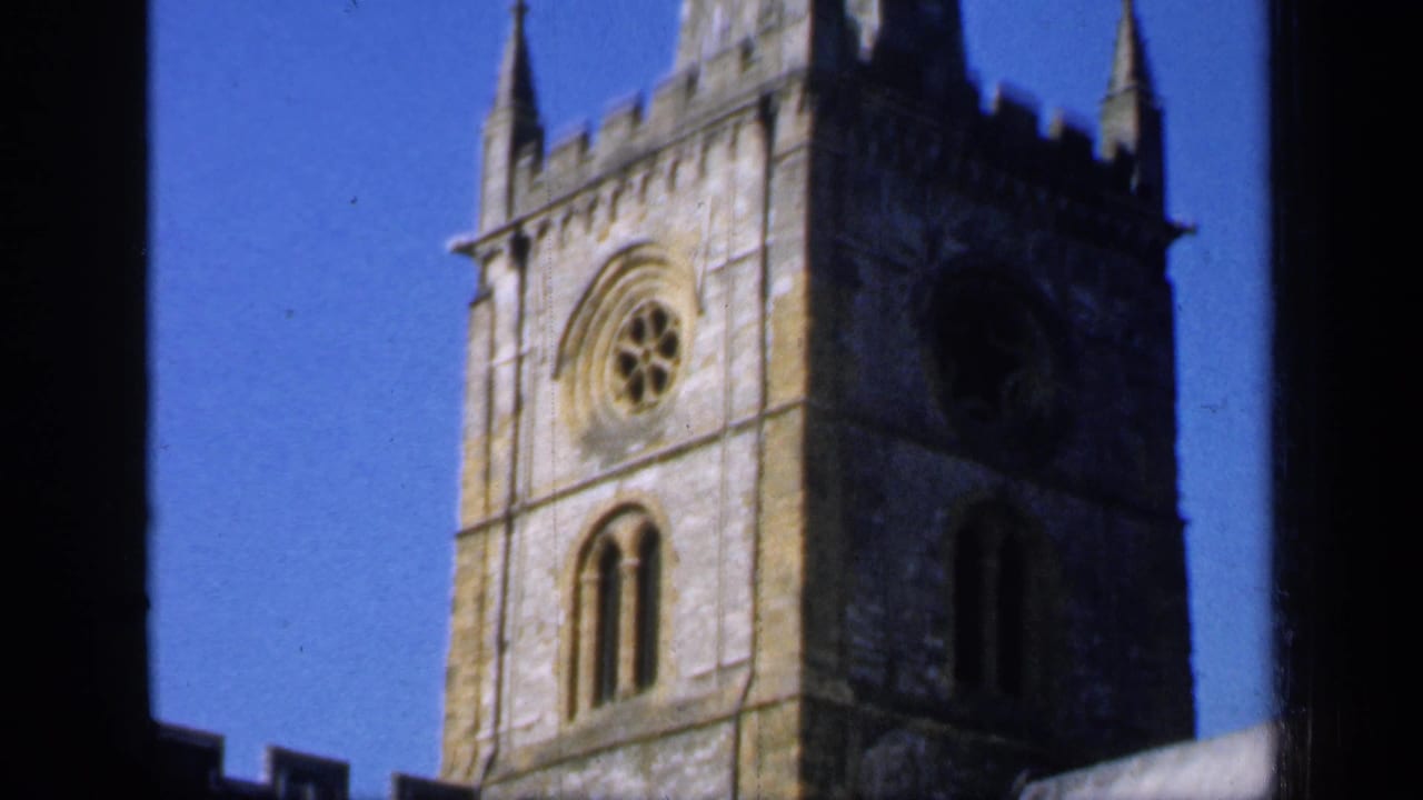 1949 England 8mm frame showing the upper church tower with a rose window, arched openings and blue sky.