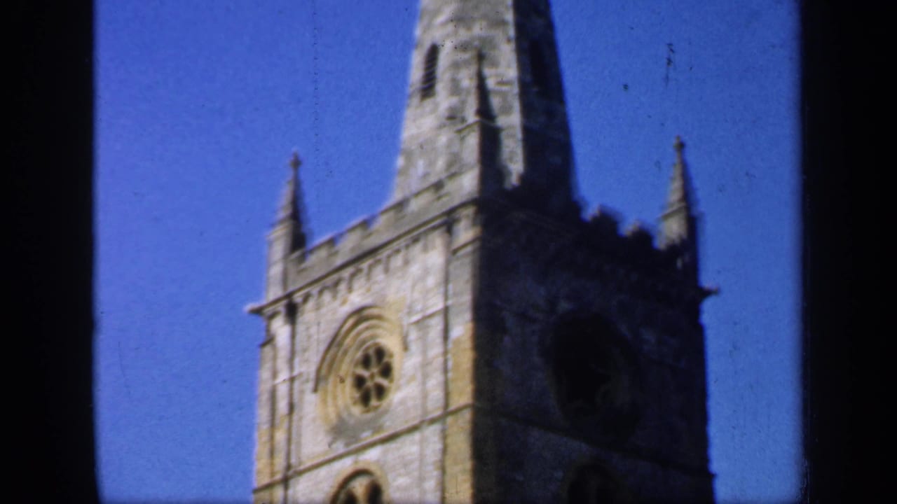 Church tower and spire rising into blue sky, partly divided by dark film borders.