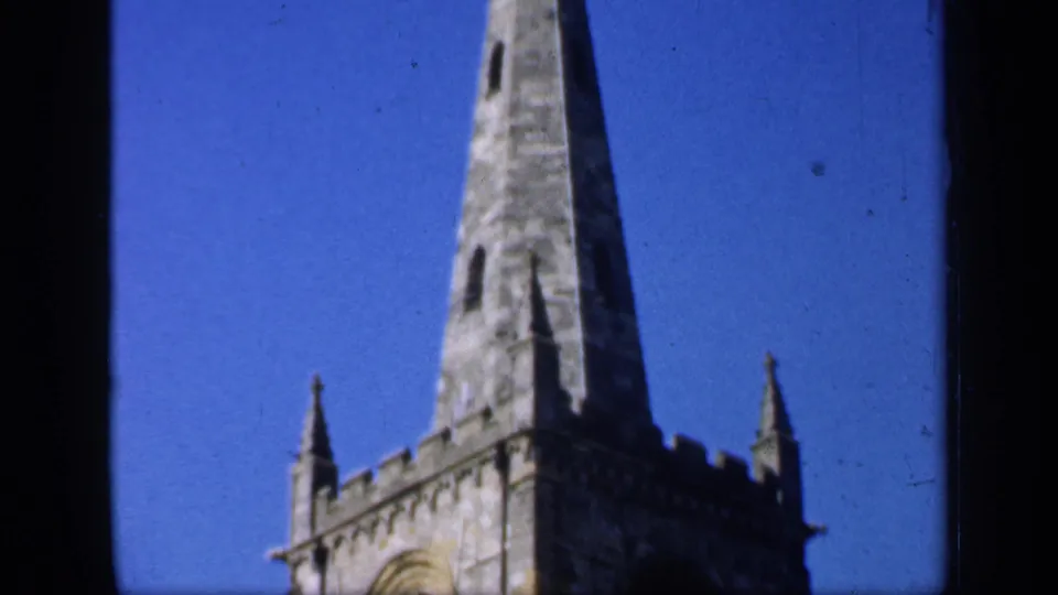 1949 England 8mm frame emphasizing the tall pointed spire above the Gothic church tower.