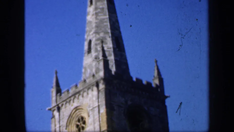 Low-angle 1949 England view of a Gothic-style church tower with a rose-like circular window and tall spire.