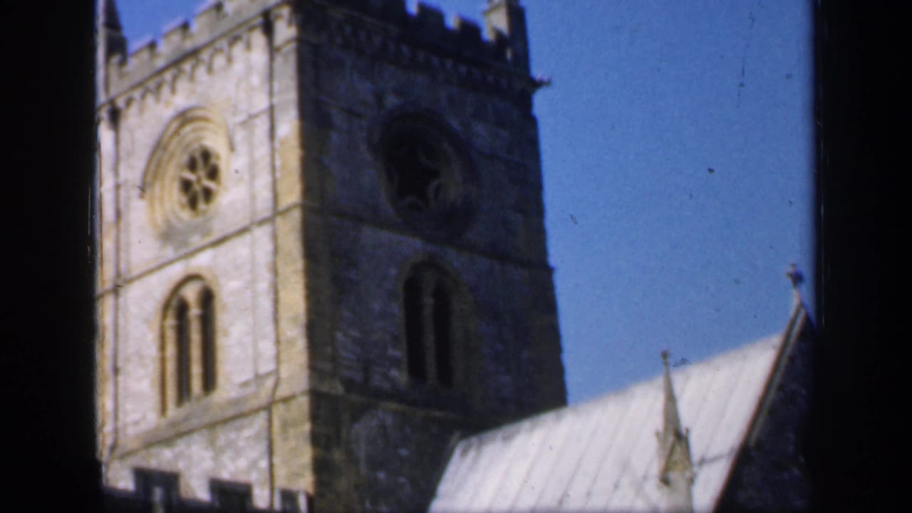 Stone church tower and roof seen through dark window framing.