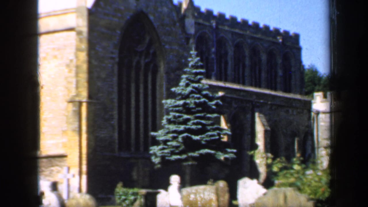Gothic stone church with a tall evergreen and several headstones in the foreground.