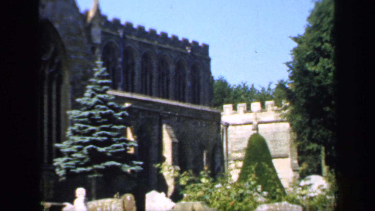 Stone Gothic churchyard with tombstones, trees, clipped greenery, and blue sky.