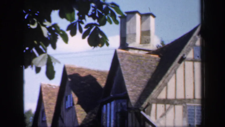 1949 England frame with tiled roofs, chimneys, timber framing, and leafy branches partly blocking the village architecture.