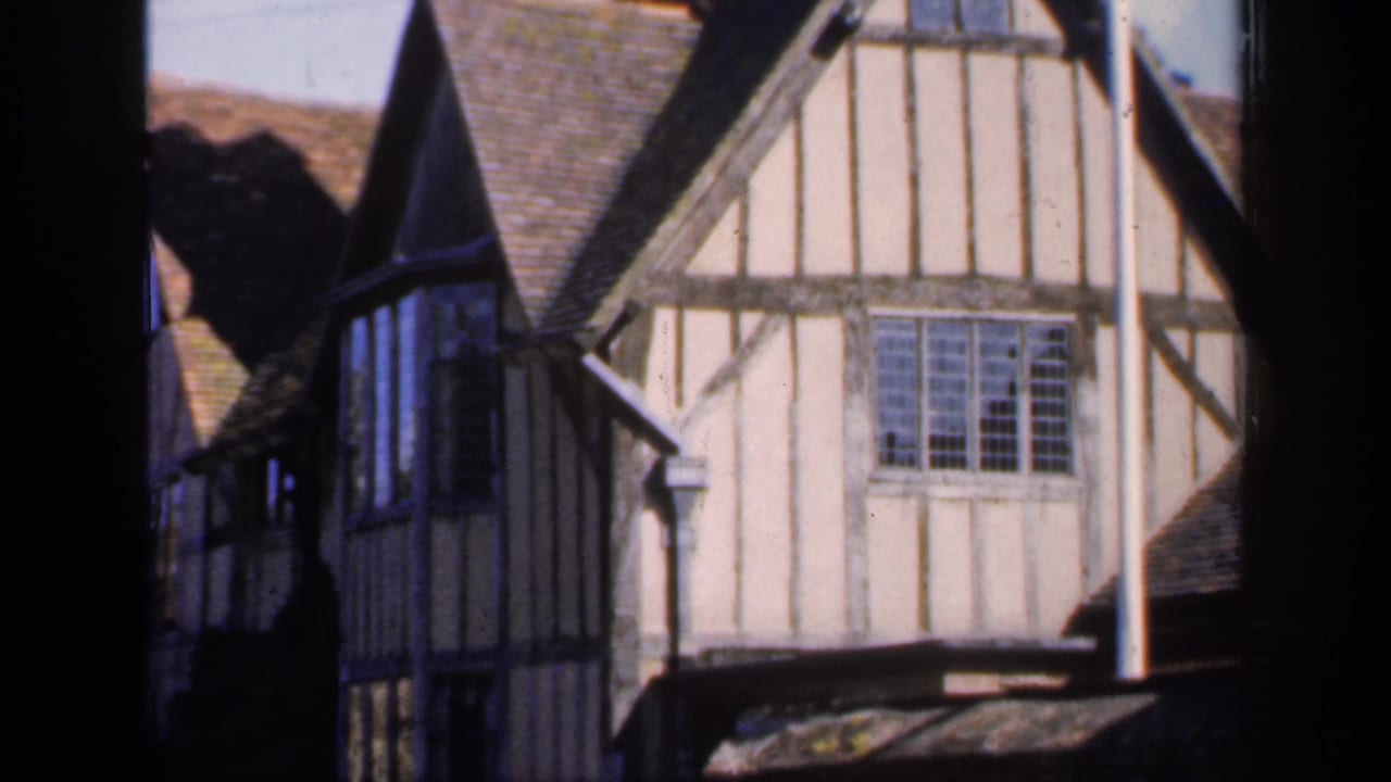 1949 England frame showing adjoining half-timbered house fronts, steep tiled roofs, and a prominent leaded window.