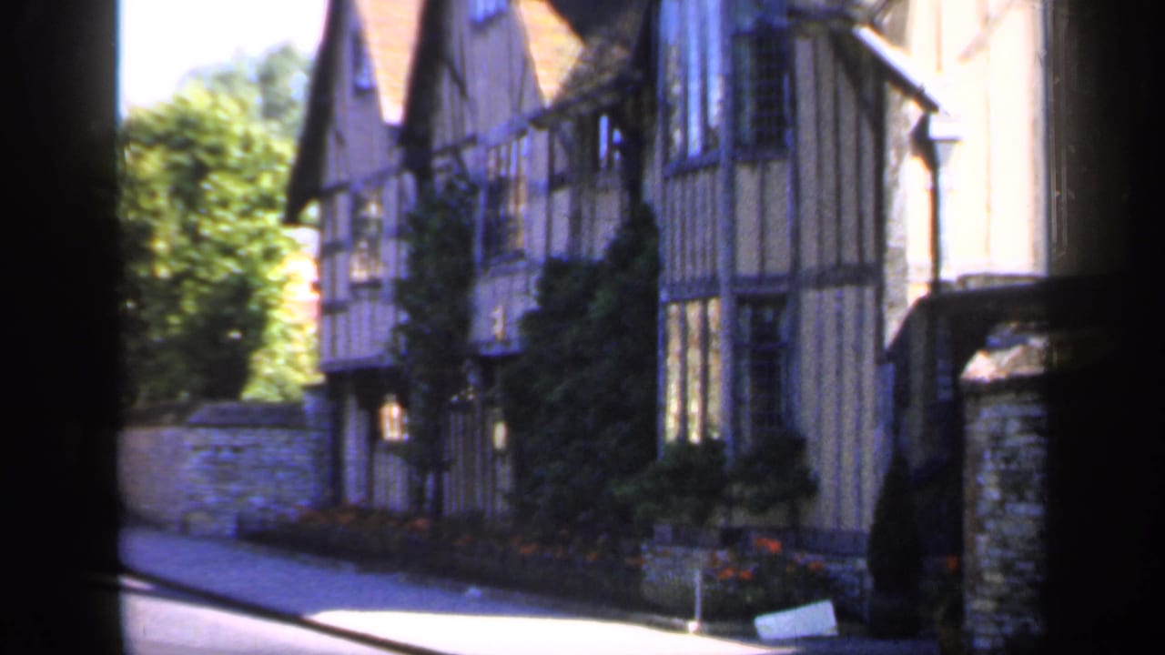 Sunlit street beside timber-framed buildings and a stone wall.