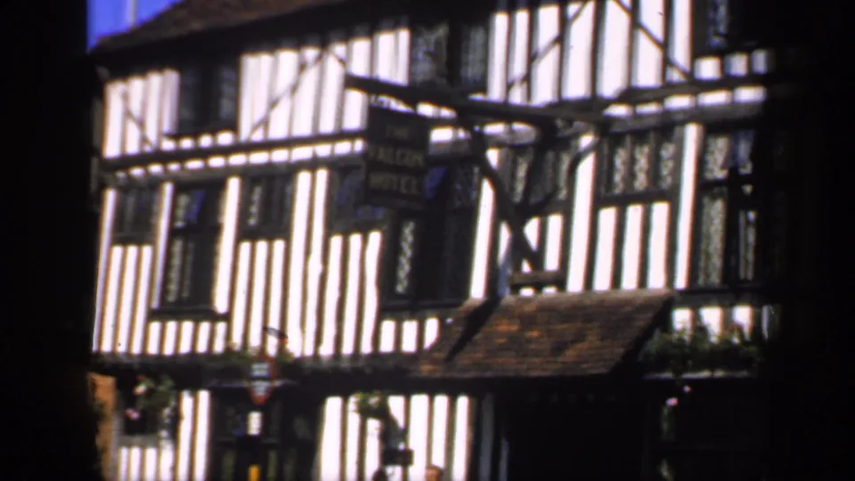 1949 England frame showing a close moving-vehicle view of The Falcon Hotel sign and timber-framed exterior.