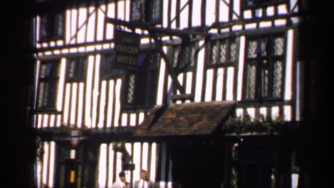 Timber-framed hotel facade with dark foreground obstruction and two adults near the doorway.