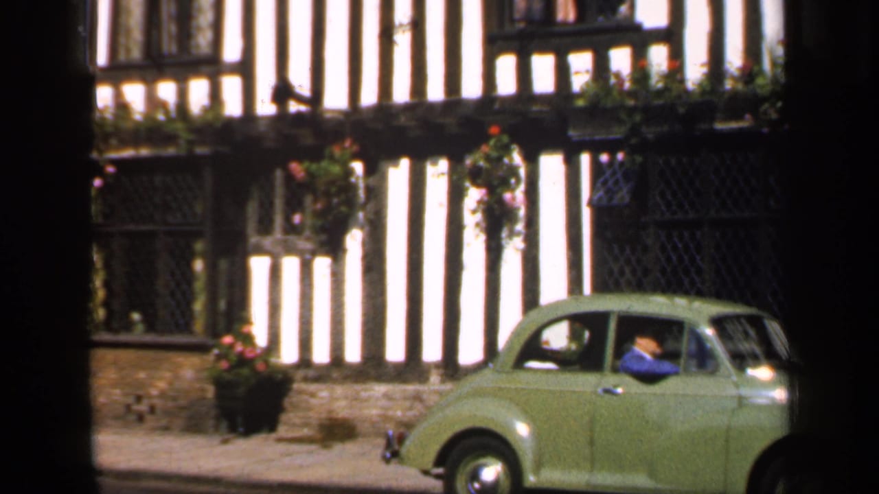 Green vintage car beside timber-framed building and dark leaded windows.