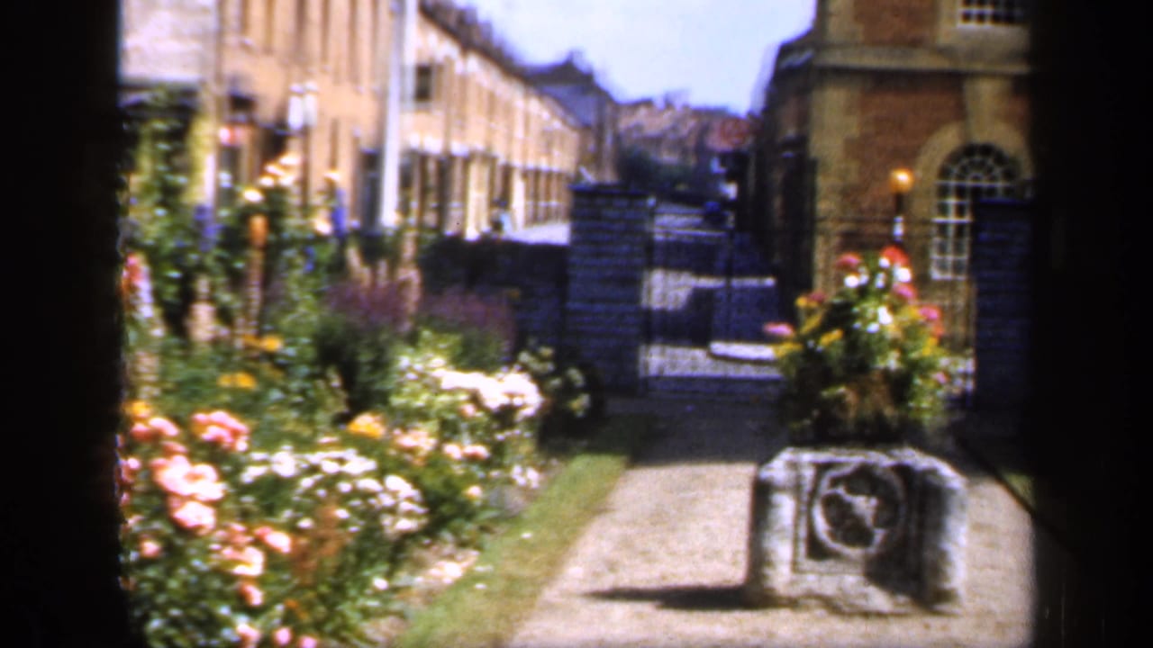Garden path with flower beds, brick building, arched window, gate, and stone marker.