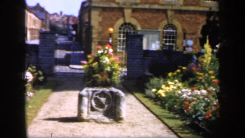 Soft 8mm frame from England in 1949 showing a garden path, stone marker, brick wall, arched windows, and flowers.