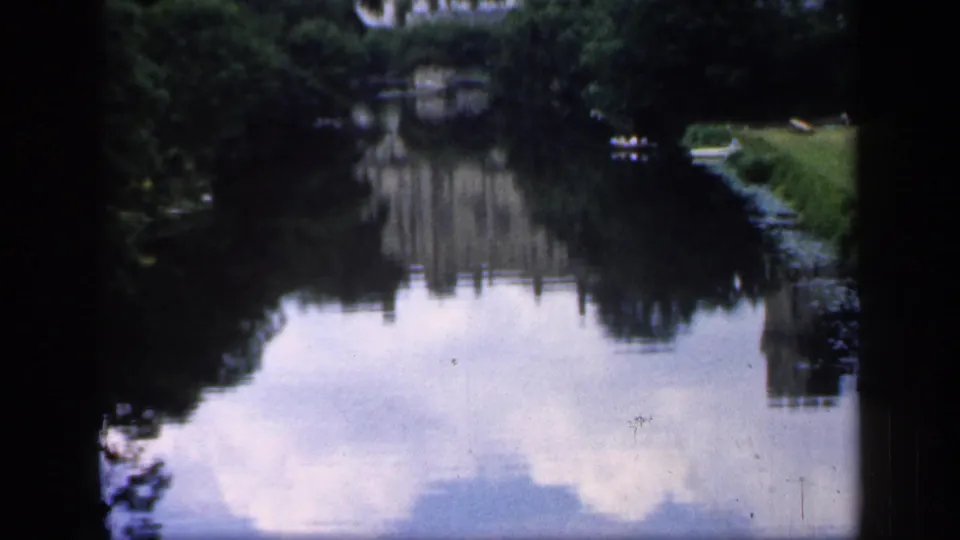 A quiet pond reflects trees, sky, and banks in the England 1949 8mm park footage.