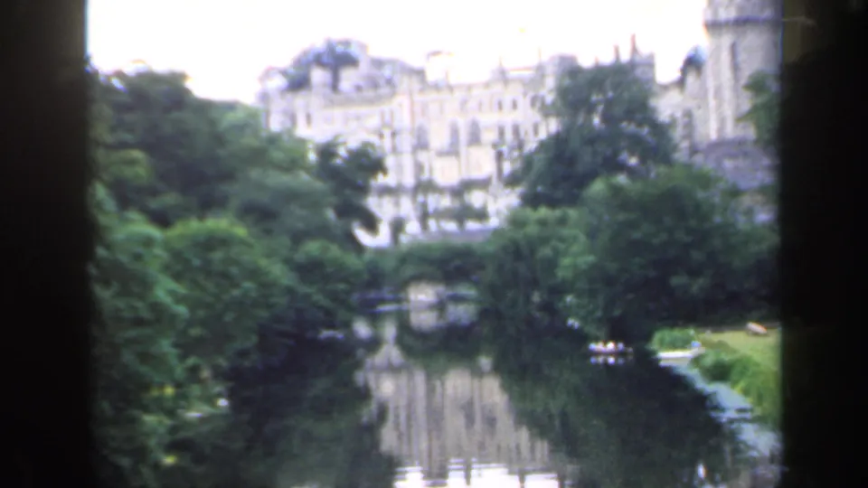 1949 England 8mm frame with a large historic building, dense greenery, river reflections, and small boats in the distance.