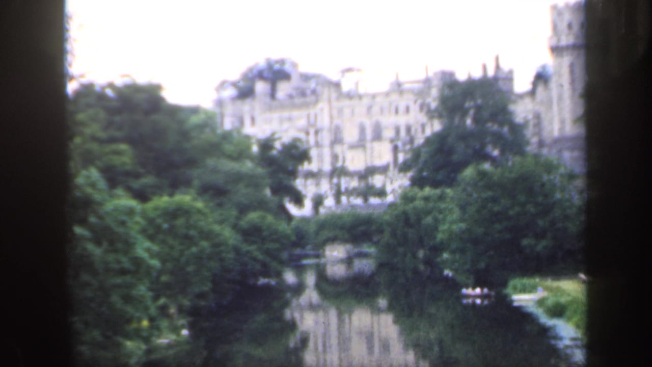 Distant castle across a river, partly framed by dark film edges and trees.