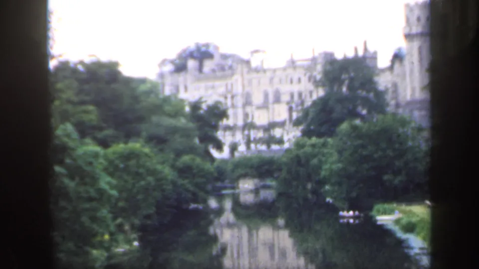 1949 England 8mm view of a pale stone castle beyond trees and a calm river, with dark vertical frame edges.