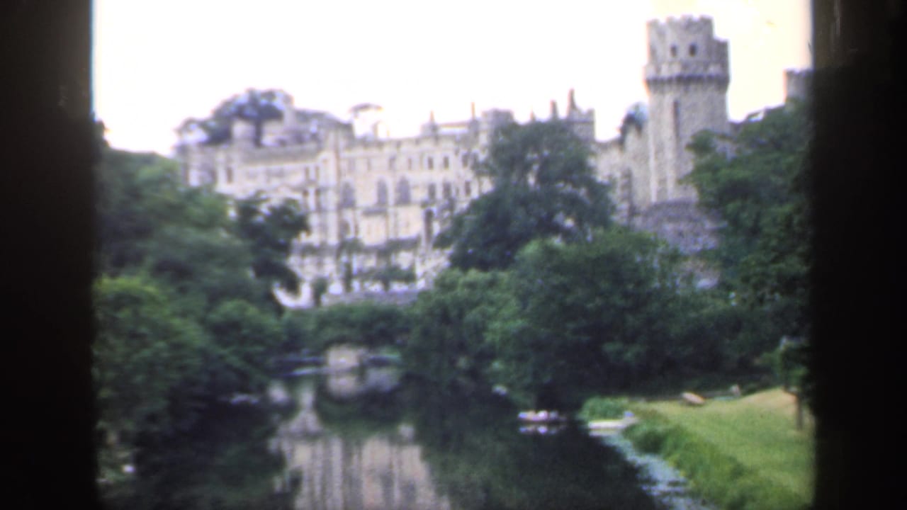 1949 England home-movie frame showing a castle tower above dense greenery with river water below.