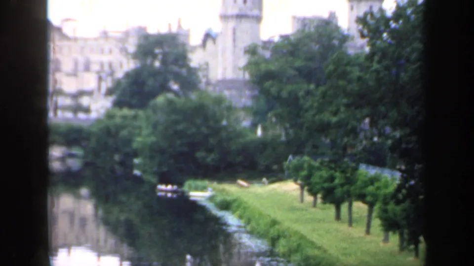 1949 England home-movie view of a wooded riverbank with castle buildings and tower partly visible behind trees.