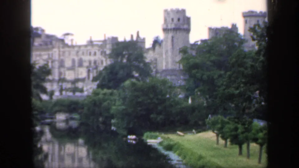 Distant 1949 England view of a castle and tower across landscaped grounds, water, and heavy tree cover.